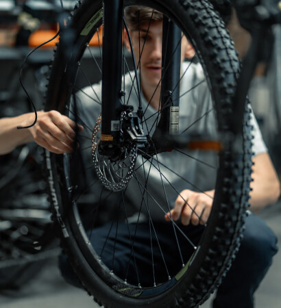 Ein konzentrierter Fahrradmechaniker inspiziert ein Fahrradvorderrad mit Scheibenbremse in einer Reparaturwerkstatt.