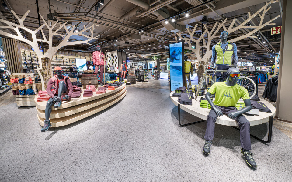 Innenansicht eines Outdoor-Ausrüstungsgeschäfts mit Schaufensterpuppen, die Wander- und Radsportbekleidung auf modernen Präsentationseinheiten präsentieren.