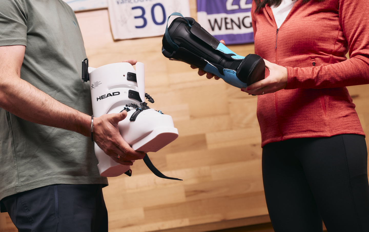 Ein Mann hält einen weißen HEAD Skischuh, eine Frau hält einen schwarzen und blauen Skischuh, in einem Wintersportgeschäft.