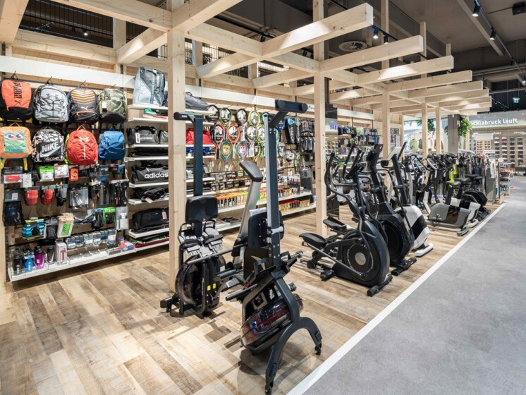 Innenansicht eines modernen Sportgeschäfts mit Reihen von Trainingsgeräten und Regalen voller Sportrucksäcke.