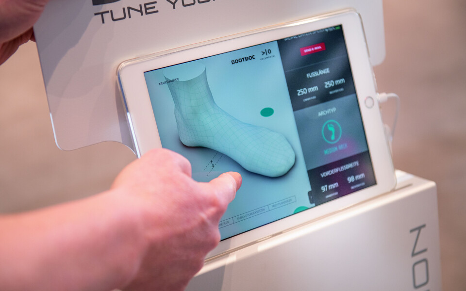 Eine Hand bedient ein Tablet, das einen 3D-Fußscan und digitale Messungen für die individuelle Sockenanpassung zeigt.